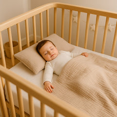 Slapende baby in een houten ledikant onder een beige mousseline deken met bijpassend kussen