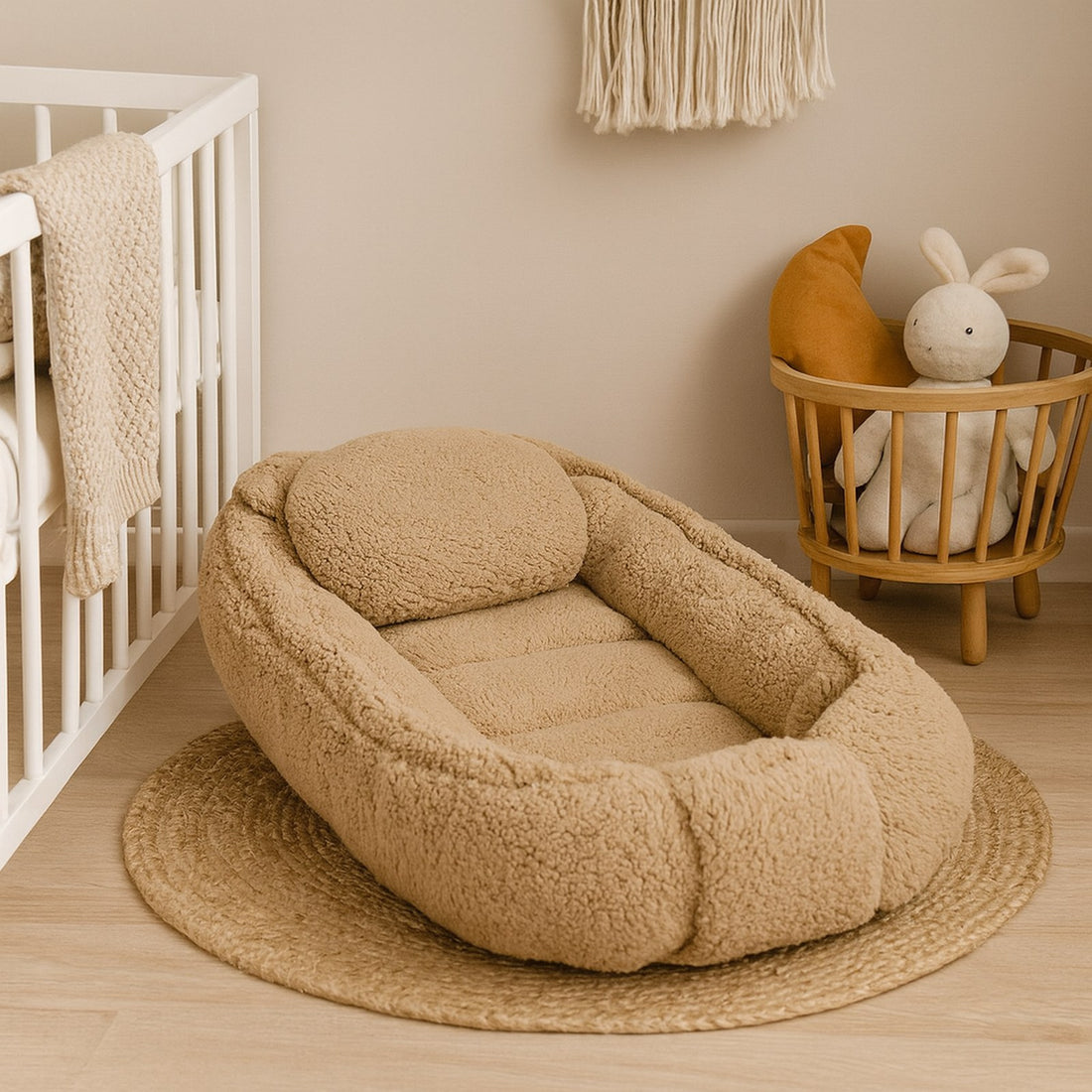 Beige babynestje van teddy bouclé op een jute vloerkleed naast een wit ledikant