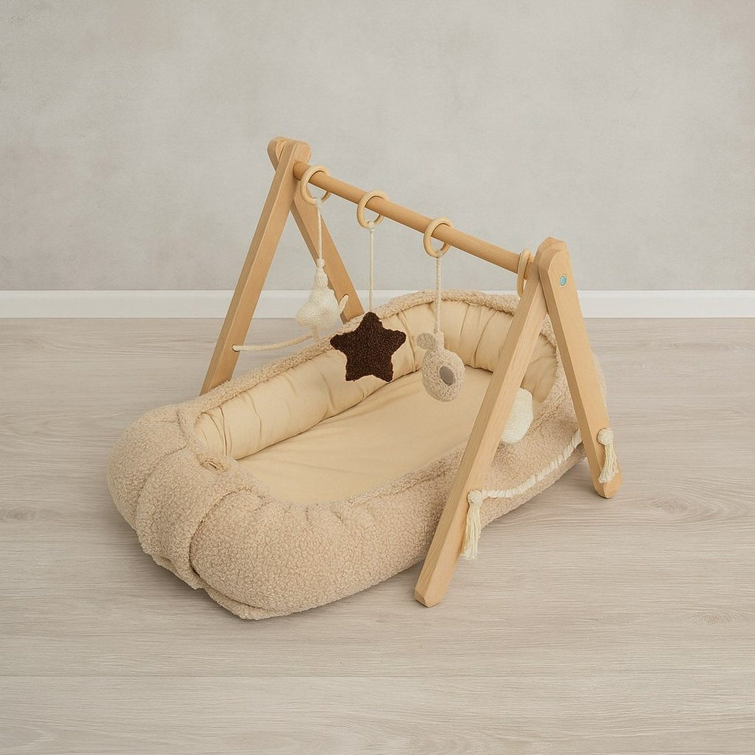 Beige babynestje van teddy bouclé met een houten babygym erboven