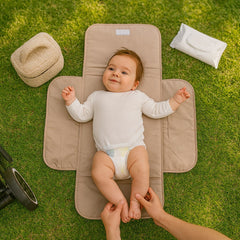 Baby op een beige opvouwbaar verschoonmatje in het gras, met billendoekjes en een bouclé mandje ernaast