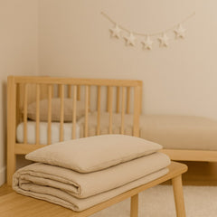 Opgevouwen beige mousseline beddengoed met kussen op een houten bankje voor een ledikant